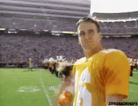 Man in Yellow Jersey Standing on Football Field in Front of Stadium