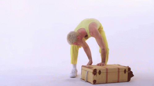 Man in Yellow Pants Bending Over Brown Suitcase