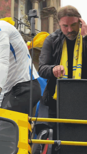 Man in Yellow Scarf With Letter E Standing in Front of Speaker