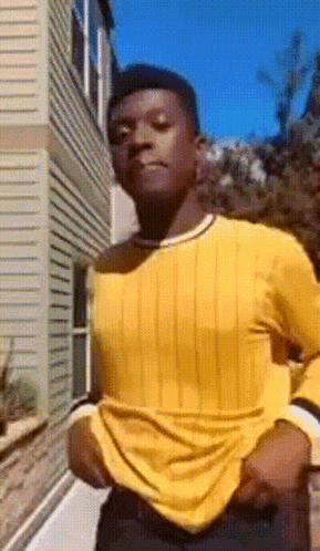 Man in Yellow Shirt and Black Pants Standing in Front of Building