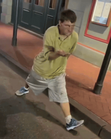 Man In Yellow Shirt And Grey Shorts On Sidewalk GIF