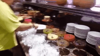 Man in Yellow Shirt in Front of Cakes and Plates