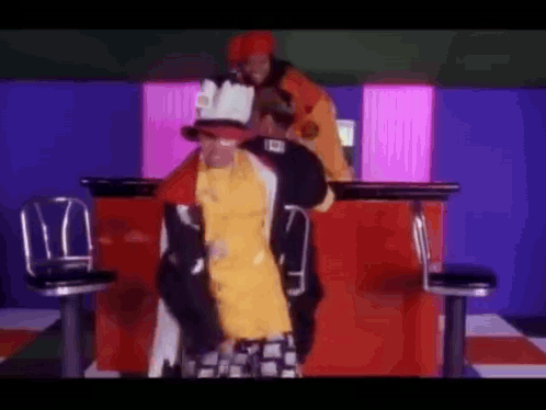 Man In Yellow Shirt Next To Man In Red Jacket GIF