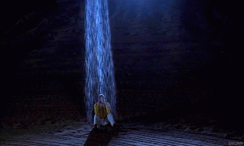Man in Yellow Shirt Under Waterfall in Dark Room