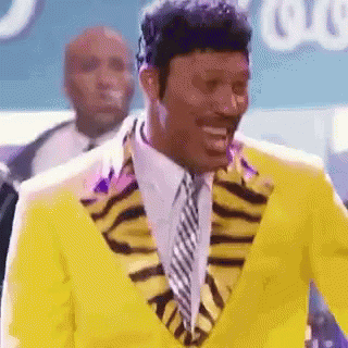 Man in Yellow Suit and Tie Smiling in Front of Crowd