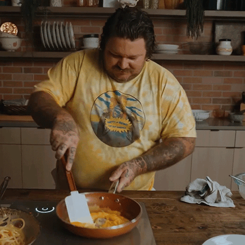 Man in Yellow Tie Dye Shirt Stirring Skillet