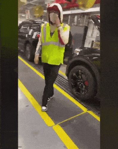 Man In Yellow Vest And Helmet On Conveyor Belt With Car GIF