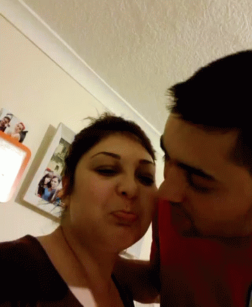 Man Kissing Woman On Cheek In Front Of Pictures GIF