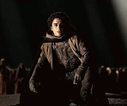 Man Kneeling in Dark Wearing Cape