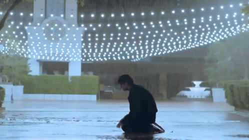 Man Kneeling in Rain Under Lights
