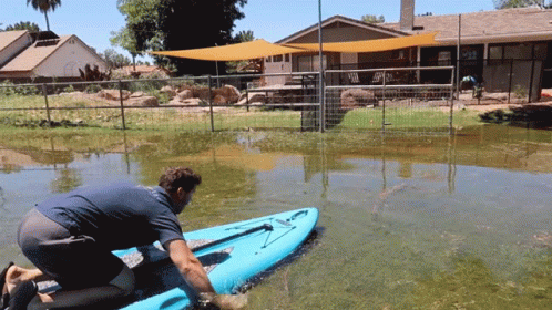 Man Kneeling On Blue Kayak In Flooded Area GIF