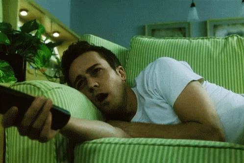 Man Laying On Green And White Striped Couch Holding Remote GIF