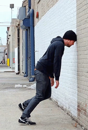 Man Leaning Against White Brick Wall in Alleyway