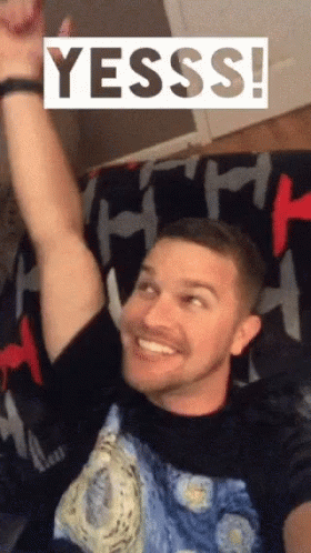 Man on Couch With Arm Up Saying Yesss