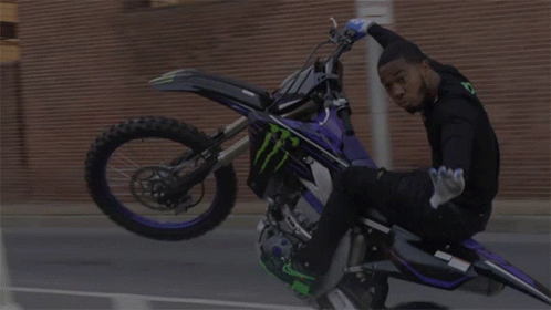 Man on Dirt Bike Doing Handstand in Front of Stop Sign