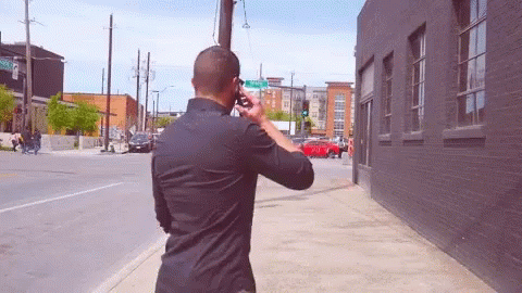 Man on Phone Walking by Green Street Sign