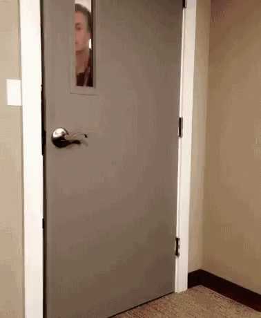 Man Peeking Out Of Gray Door With Window GIF