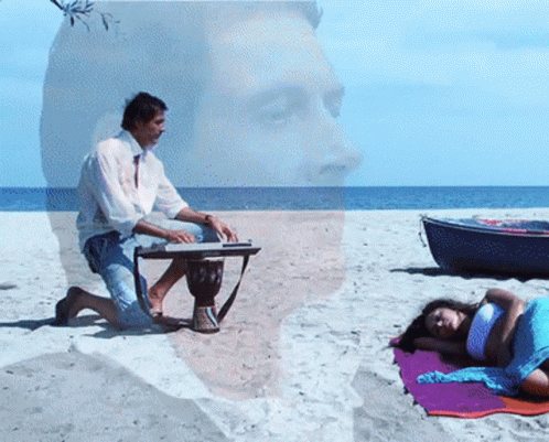 Man Playing Drum On Beach With Woman Laying On Towel GIF