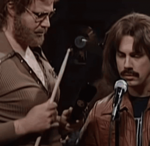 Man Playing Drums Next to Man With Mustache