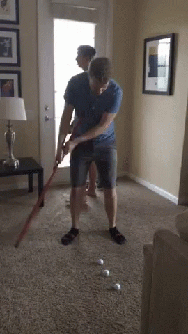 Man Playing Golf in Living Room While Another Watches