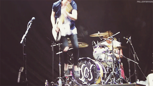 Man Playing Guitar in Front of Drum Set Saying SOS