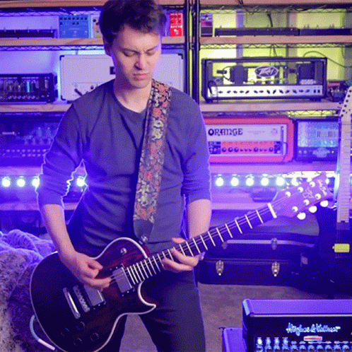 Man Playing Guitar in Front of Stack of Orange Amps