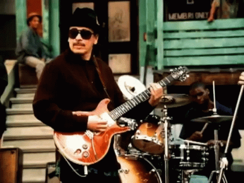 Man Playing Guitar in Sunglasses and Hat by Drum Set