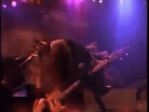 Man Playing Guitar on Stage with Purple Lights