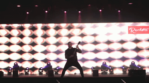 Man Playing Guitar on Stage With Rockstar Sign