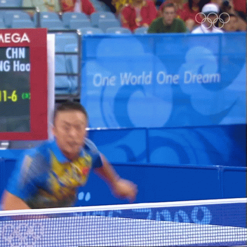 Man Playing Ping Pong in Front of One World One Dream Sign