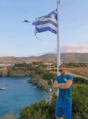 Man Posing Beside Pole Of Greece Flag GIF