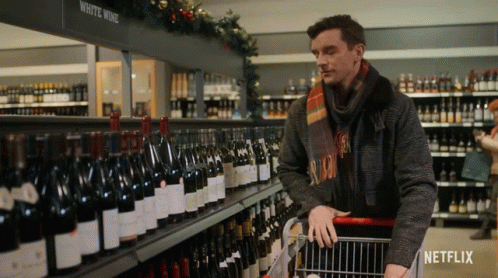 Man Pushing Shopping Cart Past White Wine Shelf GIF