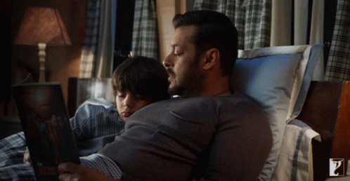 Man Reading Book To Boy Lying On Stomach GIF