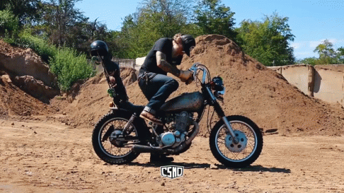 Man Riding Motorcycle in Dirt Field with Word Csnd