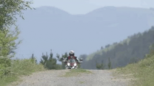 Man Riding Motorcycle on Dirt Road with Mountains