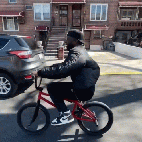 Man Riding Red Bike Down Street Past Brick Building