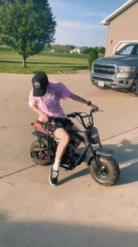 Man Riding Small Motorcycle Beside Ram Truck