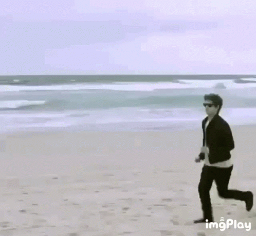 Man Running on Beach Next to Yellow Sign