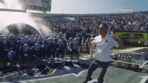 Man Running on Football Field With Players Behind Him
