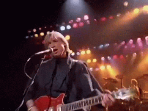 Man Singing Into Microphone and Playing Guitar on Stage