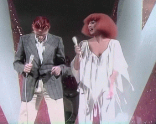 Man Singing into Microphone Beside Woman in White Dress