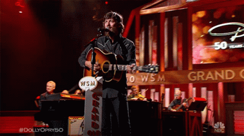 Man Singing Into Microphone Holding Guitar With WSM Sign