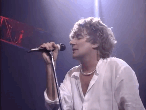 Man Singing Into Microphone on Stage in Dark Room