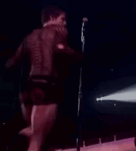 Man Singing Into Microphone On Stage In Shorts GIF