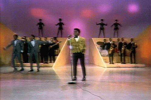 Man Singing Into Microphone on Stage With Band