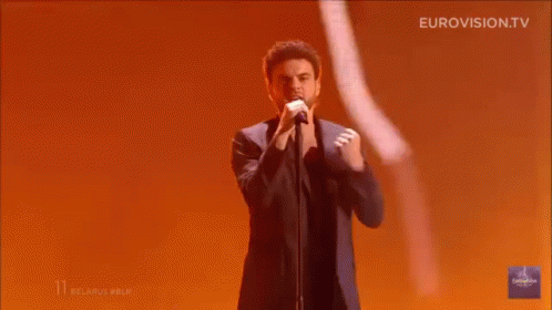 Man Singing on Stage With Hands in Air