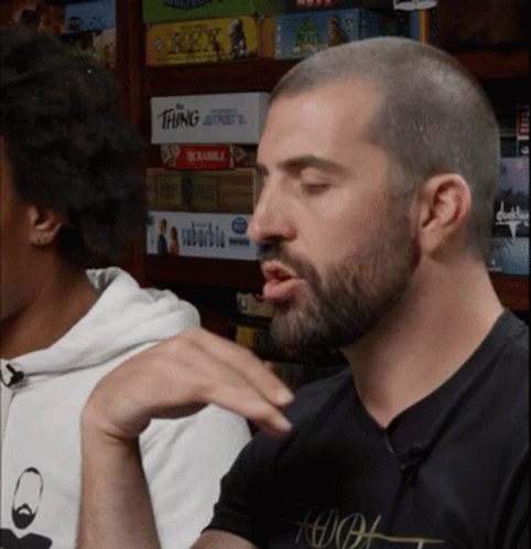 Man Sitting at Board Game Shelf With Scrabble
