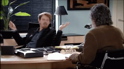 Man Sitting at Desk Talking to Another