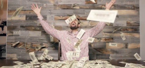 Man Sitting At Table With Money Falling From Sky GIF