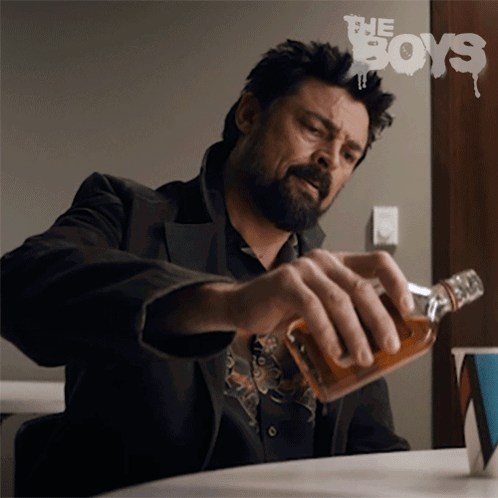 Man Sitting at Table With Whiskey Bottle in Front of The Boys Sign
